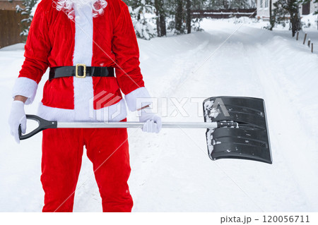 Santa Claus cleans snow with shovel in winter outdoors after a snowfall. Cleaning the streets in the village, clearing the passage for cars, difficult weather conditions for Christmas and New Year Santa Claus cleans snow with shovel in winter outdoors after a snowfall. Cleaning the streets in the village, clearing the passage for cars, difficult weather conditions for Christmas and New Year 120056711
