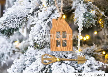 Key and tiny house keychain in hand on background fairy lights Christmas tree. gift for New Year, Christmas. Building, design, project, moving, insurance, mortgage, rent and purchase real estate. 120056851