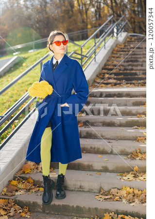 Portrait of stylish smiling young woman walking in park, wearing blue coat. Autumn trendy fashion 120057344