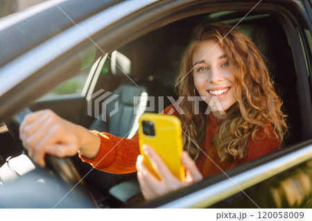 Portrait of a young woman sitting in a car in the driver's seat looking into a smartphone. Portrait of a young woman sitting in a car in the driver's seat looking into a smartphone. 120058009