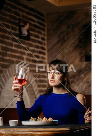 Woman enjoying sushi with wine in a stylish restaurant, creating a refined dining experience Woman enjoying sushi with wine in a stylish restaurant, creating a refined dining experience 120058503
