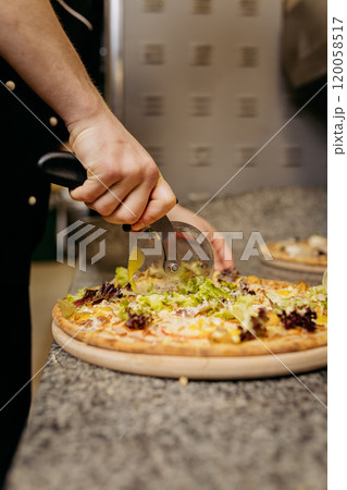 Chef slicing fresh vegetable pizza with pizza cutter on granite countertop for a perfect serving 120058517