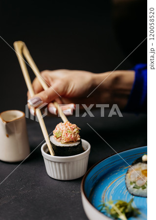 Hand dipping a sushi roll with crab topping into a small soy sauce dish 120058520
