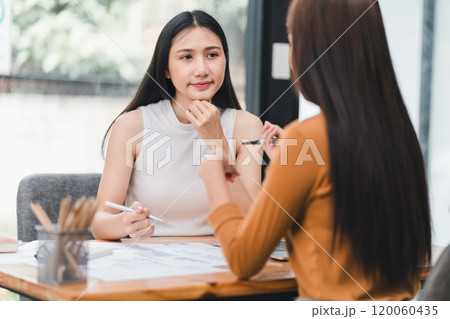 Two young Asian businesswomen discuss an investment project and planning strategy, Talk together while working on laptop computer in the office. Two young Asian businesswomen discuss an investment project and planning strategy, Talk together while working on laptop computer in the office. 120060435