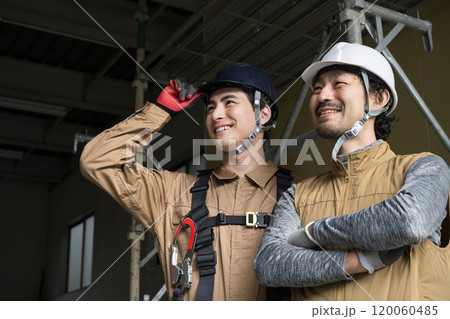 鳶職や屋外の安全帯ハーネスをつけた作業のガテン系作業員二人の見上げる笑顔　あおりのコピースペースあり 120060485