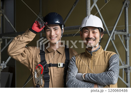 鳶職や屋外の安全帯ハーネスをつけた作業のガテン系作業員二人の見上げる笑顔　 120060486