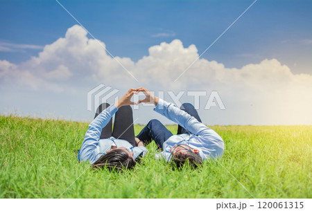 Happy couple lying on grass making heart shape, Couple on grass making heart shape with hands, Young couple lying on grass making love symbol with hands 120061315