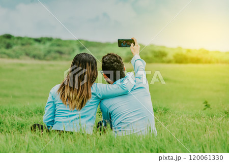 Couple in love taking a selfie sitting in a beautiful field. Young happy couple taking a selfie sitting in the field 120061330