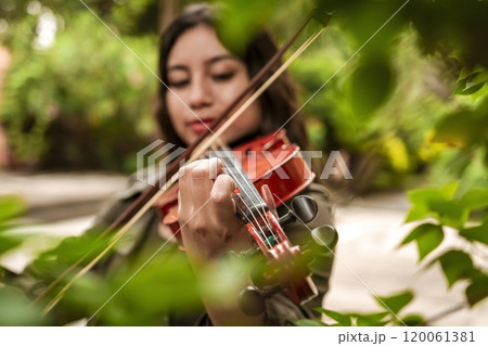 Girl with her violin playing a melody outdoors, Concept of smiling female violinist. Attractive girl playing the violin outdoors. Portrait of a girl playing the violin outdoors 120061381