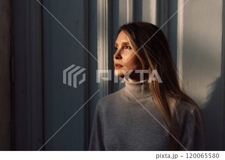 A woman with long hair is standing in front of a white door. She is wearing a sweater and she is looking out the window. A woman with long hair is standing in front of a white door. She is wearing a sweater and she is looking out the window. 120065580