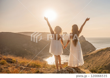 Two women are standing on a hill overlooking the ocean. They are holding hands and looking out at the water. The scene is peaceful and serene, with the sun shining brightly in the background. Two women are standing on a hill overlooking the ocean. They are holding hands and looking out at the water. The scene is peaceful and serene, with the sun shining brightly in the background. 120066535