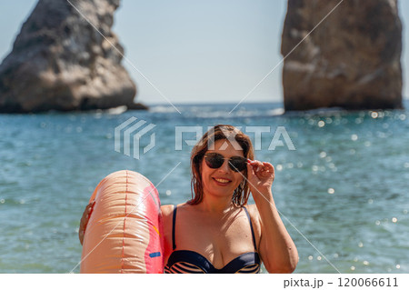 Woman, Beach, Lebanon: Smiling woman in a swimsuit holding a floatie on the beach in front of the iconic rock formations of Raouche, Beirut. Woman, Beach, Lebanon: Smiling woman in a swimsuit holding a floatie on the beach in front of the iconic rock formations of Raouche, Beirut. 120066611