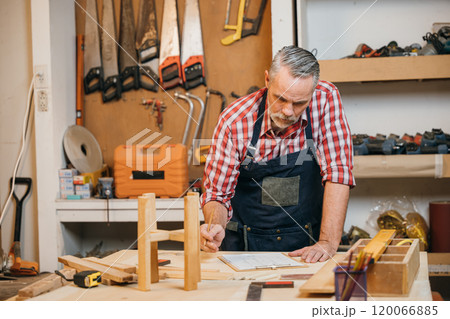 Man in plaid shirt and overalls working on a wooden project in his workshop, drawing on clipboard with pencil. Surrounded by tools and wood, woodworking and DIY craftsmanship, National Carpenters Day Man in plaid shirt and overalls working on a wooden project in his workshop, drawing on clipboard with pencil. Surrounded by tools and wood, woodworking and DIY craftsmanship, National Carpenters Day 120066885