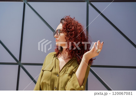 Portrait of a woman standing near a supermarket building. Caucasian model with long brunette hair, wears sunglasses and a khaki dress. 120067081