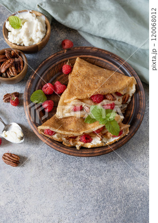 Tasty homemade sweet crepes stuffed with raspberries and cream cheese on a gray stone background. Thin pancakes, blini. Sweet dessert. Copy space. Tasty homemade sweet crepes stuffed with raspberries and cream cheese on a gray stone background. Thin pancakes, blini. Sweet dessert. Copy space. 120068012