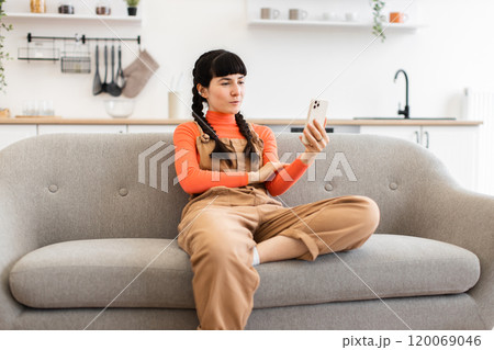 Young woman having video call while sitting on a comfortable sofa Young woman having video call while sitting on a comfortable sofa 120069046