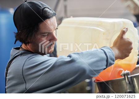 Portrait of concentrated male factory worker pouring apple juice from plastic container into tank making craft cider while monitoring product quality in workshop, copy space 120071625