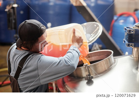 High angle shot of male production worker pouring apple juice from plastic container into stainless steel tank making craft cider in workshop of factory, copy space 120071629