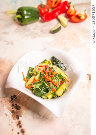 Fresh cucumbers, bell peppers, and herbs on white plate, pink background Fresh cucumbers, bell peppers, and herbs on white plate, pink background 120071657