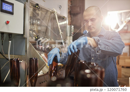Medium shot of concentrated male production operator in protective gloves carefully sterilizing glass bottles at craft cider or beer factory, copy space Medium shot of concentrated male production operator in protective gloves carefully sterilizing glass bottles at craft cider or beer factory, copy space 120071760