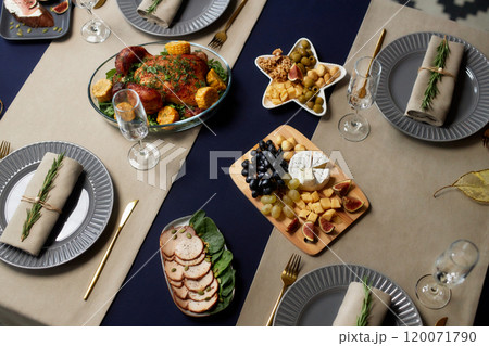 High angle shot of cheese platter on wooden board and roasted chicken served on festive table setting decorated with champagne glasses and minimalist dishware on Christmas Eve, copy space 120071790