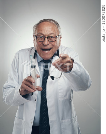 Youll get a lollipop after this injection. Shot of an elderly male doctor holding a syringe for injection in a studio against a grey background. 120072829