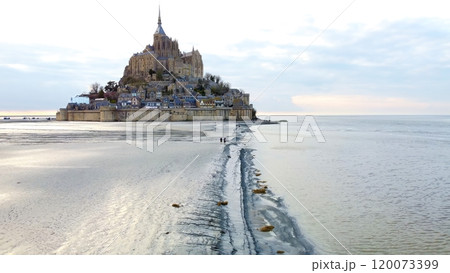 Visitors approaching Mont Saint Michel, Normandy, France across tidal flats 120073399