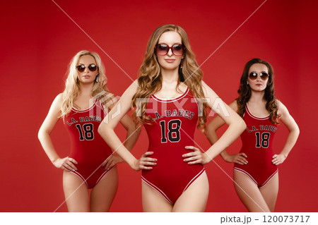 Three women in red swimsuits on a red background Three women in red swimsuits on a red background 120073717