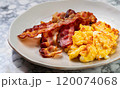 macro shot of fried bacon and scrambled eggs on a plate on a white marble serving table 120074068