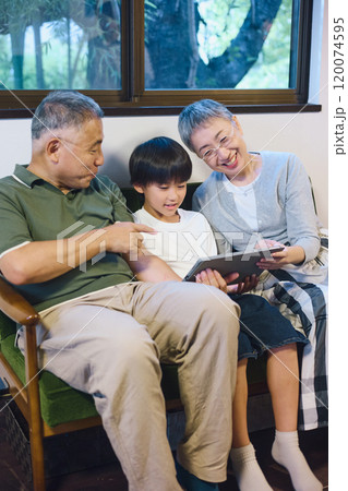 家でタブレットを一緒に楽しむ孫と祖父母 120074595