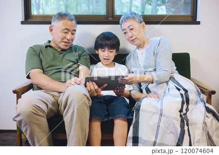 家でタブレットを一緒に楽しむ孫と祖父母 120074604