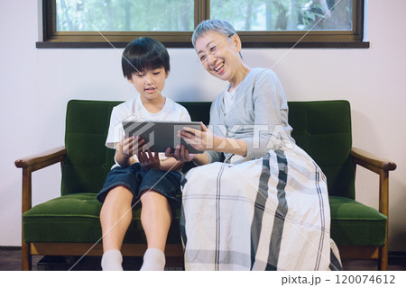 家でタブレットを一緒に楽しむ孫と祖母 120074612