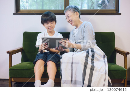 家でタブレットを一緒に楽しむ孫と祖母 120074613