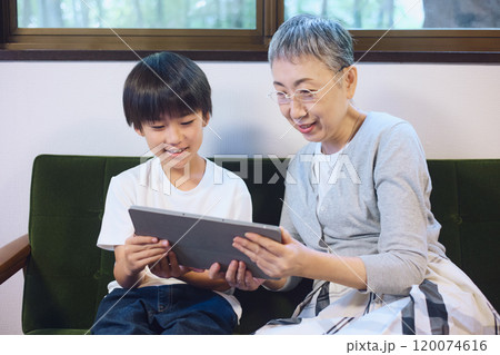 家でタブレットを一緒に楽しむ孫と祖母 120074616
