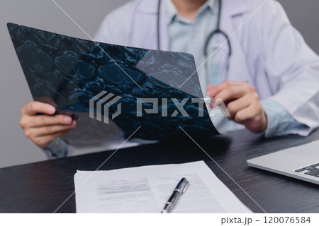 Doctor examining an X-ray image on a desk. Relevant for healthcare, medical diagnostics, radiology, and patient care content. Doctor examining an X-ray image on a desk. Relevant for healthcare, medical diagnostics, radiology, and patient care content. 120076584