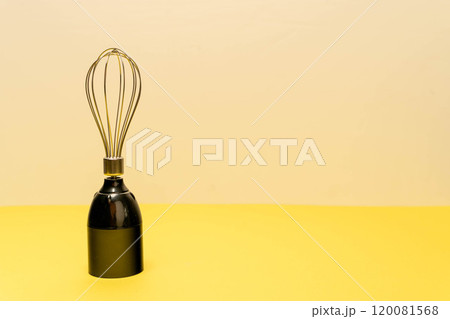 A modern whisk is positioned upright on a yellow surface A modern whisk is positioned upright on a yellow surface 120081568