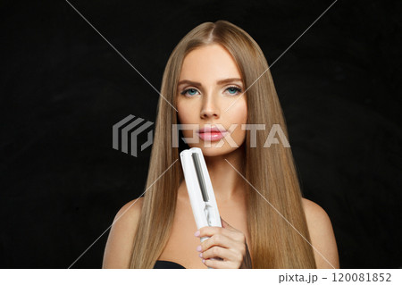 Pretty young female model woman with long brown smooth hairstyle holding straight iron.  120081852