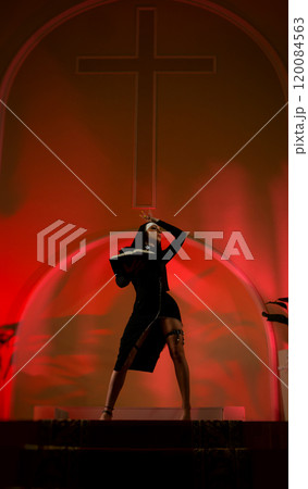 A nun girl in a sexy dress from an adult role-playing sex shop defiantly poses in a temple with a Bible book against the background of a cross 120084563