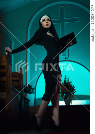 A nun in a sexy dress from an adult role-playing sex shop defiantly poses in a temple with a Bible book against the background of a cross A nun in a sexy dress from an adult role-playing sex shop defiantly poses in a temple with a Bible book against the background of a cross 120084577