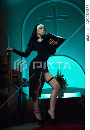 A nun in a sexy dress from an adult role-playing sex shop defiantly poses in a temple with a Bible book against the background of a cross A nun in a sexy dress from an adult role-playing sex shop defiantly poses in a temple with a Bible book against the background of a cross 120084578