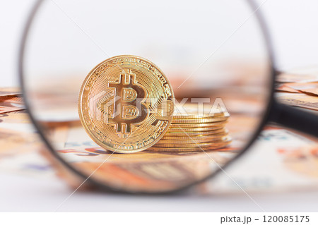 A Stack of Bitcoin Coins Visible Through a Magnifying Glass on the 50-Euro Banknotes 120085175