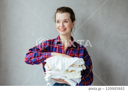 happy woman holds stack of clean white clothes in hands after washing, drying. 120085681