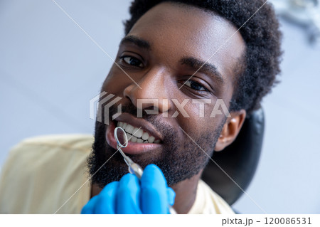 Male dentist inspecting patient’s teeth with mirror providing essential treatment during the checkup 120086531