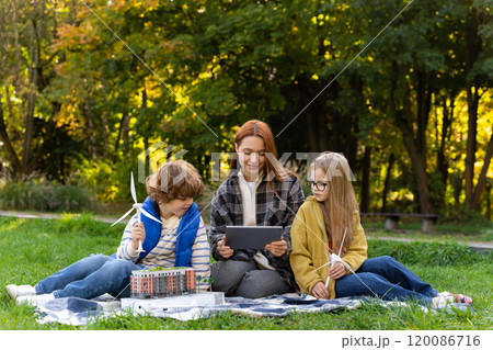 Young woman teacher using digital tablet with children in city park learning about wind turbines renewable energy Young woman teacher using digital tablet with children in city park learning about wind turbines renewable energy 120086716