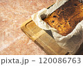 A baked cheesecake with a golden brown crust lies in a black pan on a wooden cutting board in a cozy kitchen setting 120086763