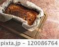 A burnt cheesecake loaf lies on a wooden cutting board surrounded by parchment paper, captured in a cozy kitchen setting 120086764