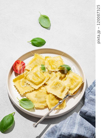 Ravioli pasta with parmesan, tomatoes and basil in a plate on a light  background with shadow 120087325
