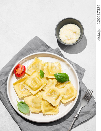 Ravioli pasta with parmesan, tomatoes and basil in a plate on a napkin on a light  background 120087326