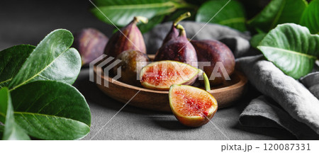 Juicy figs in a wooden plate on a dark background with leaves and a napkin close up. Juicy figs in a wooden plate on a dark background with leaves and a napkin close up. 120087331