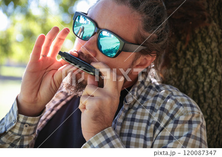 Man with Dreadlocks Ponytail in Sunglasses Playing Harmonica, Mouth Organ Man with Dreadlocks Ponytail in Sunglasses Playing Harmonica, Mouth Organ 120087347